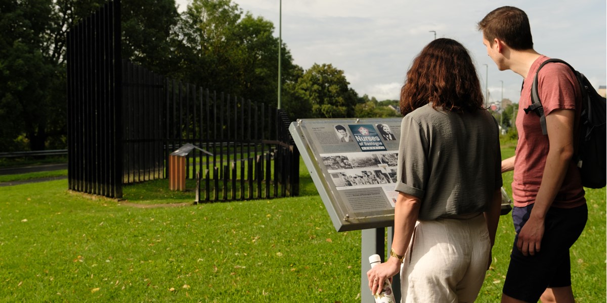 Promeneuse lisant un panneau commémoratif lors d'une randonnée mémoire au Mardasson