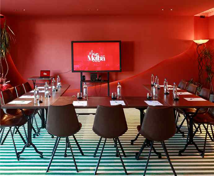 Salle de réunion rouge avec écran et tables dressées, Maison Melba Bastogne