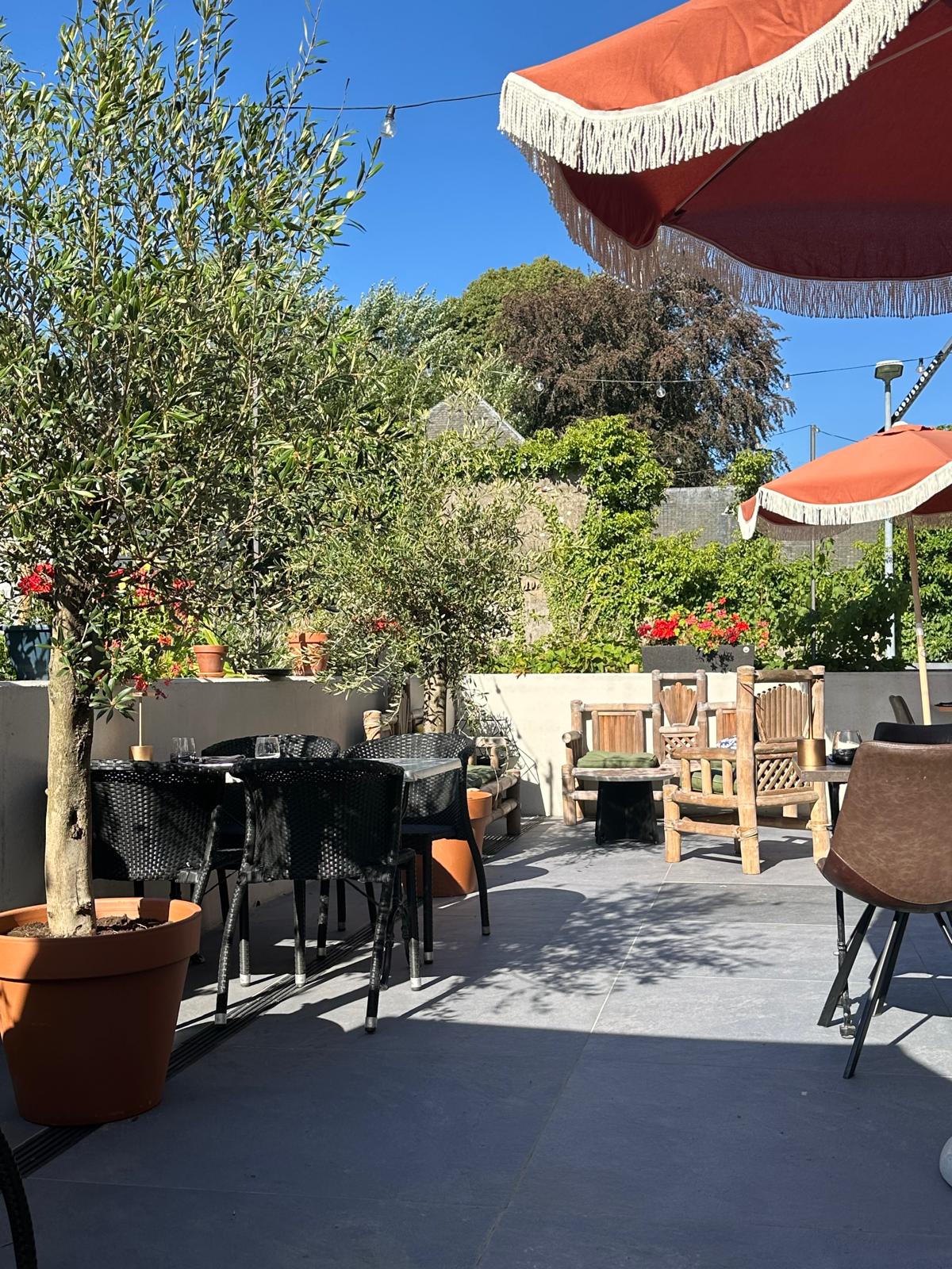 Terrasse ensoleillée avec parasols et végétation à Maison Melba